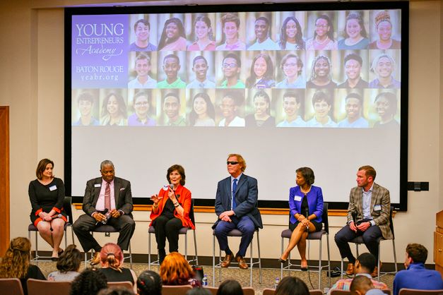 Panel of speakers on stools in front of projector screen