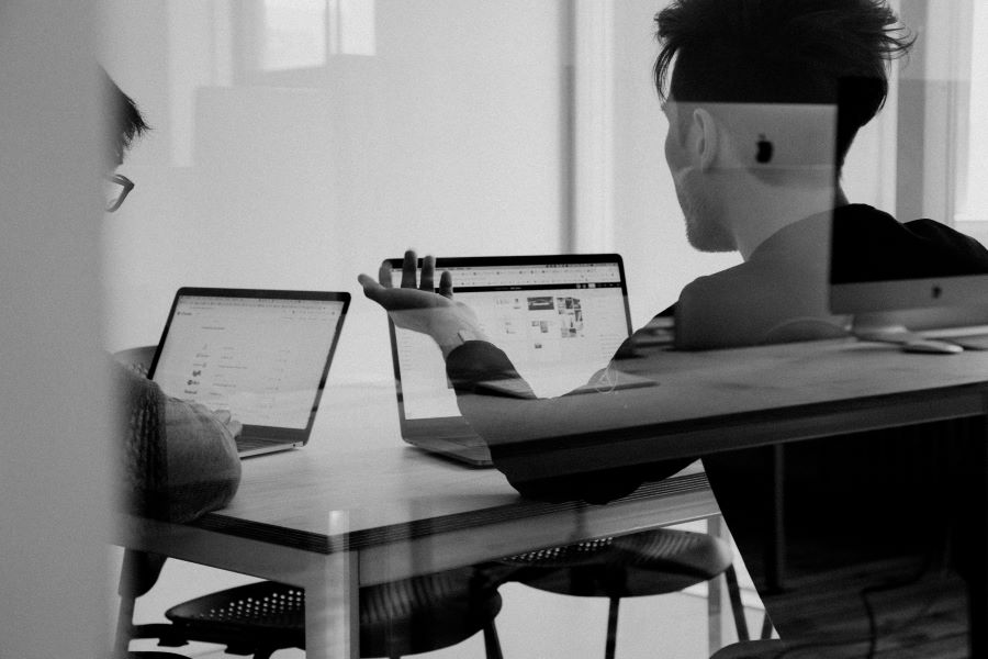 two people talk in front of laptop computers